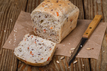 Bread, sliced into slices with the addition of flax, sesame, oats and dried carrots on a wooden table