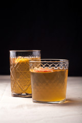 Two vintage glasses with apple cider on black background. Christmas beverages concept. Two red apples and rosemary sprig aside.  Warm backlight. Vertical composition.