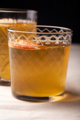 Two vintage glasses with apple cider on black background. Christmas beverages concept. Two red apples and rosemary sprig aside.  Warm backlight. Vertical composition.