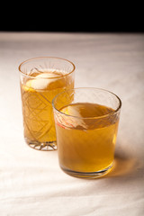 Two vintage glasses with apple cider on black background. Christmas beverages concept. Two red apples and rosemary sprig aside.  Warm backlight. Vertical composition.