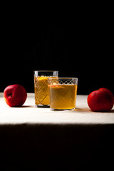 Two vintage glasses with apple cider on black background. Christmas beverages concept. Two red apples and rosemary sprig aside.  Warm backlight. Vertical composition.