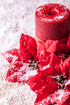 Christmas decoration, poinsettia and red decorative candle, sprinkled with snowflakes.