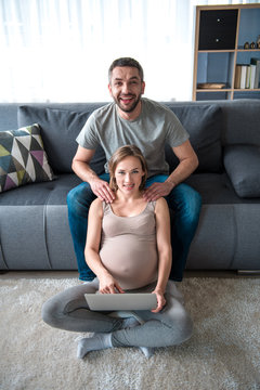 We are happy together. Full length portrait of joyful married couple relaxing at home together. Pregnant woman is getting massage while using laptop