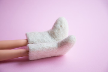 Fototapeta na wymiar woolen warm winter shoes valenki on the doll feet on a pink background. the concept of winter. winter shoes
