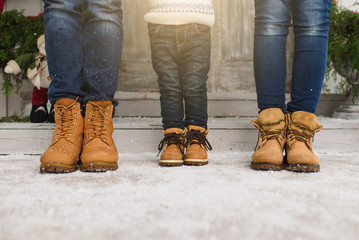 Legs of parents with little son. Child boy in sweater staying near porch snow steps at light house...