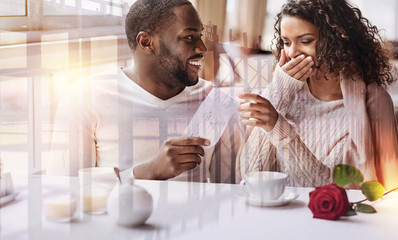 Planning future travel. Close up of young positive man showing flight tickets while his girlfriend covering her face and expressing surprise