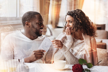 Always together. Young delighted man holding flight tickets in hand and being pleased while his girlfriend showing surprise and interest on her face