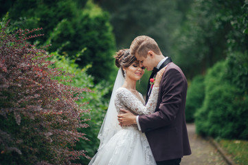 Beautiful couple of happy stylish newlyweds on a walk in the sunny summer park or garden on their wedding day