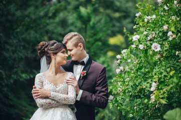 Beautiful couple of happy stylish newlyweds on a walk in the sunny summer park or garden on their wedding day