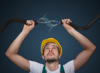 Young electrician holds cables in hands and connecting them. Lightning and electricity around.