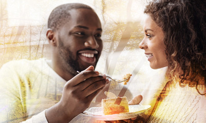 Looking tasty. Close up of African American holding a fork with dessert while looking at his woman and smiling