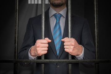 Businessman or politician behind bars in prison cell.