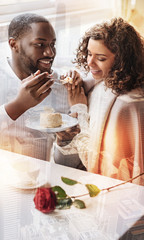 Positive day. Young pleasant couple sitting in the cafe while enjoying tasty cake and showing bright emotions