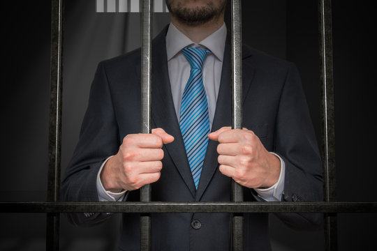 Businessman or politician behind bars in prison cell.