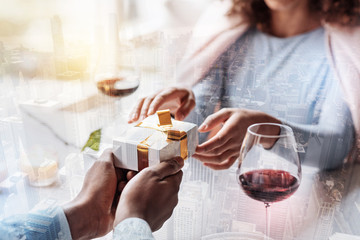Expressing love. Close up of young man giving a present to his girlfriend while sitting at the table and enjoying romantic atmosphere