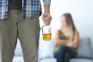 Man with bottle of alcohol and blurred woman at home