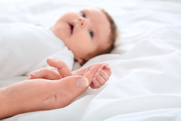 Baby holding mother's hand on bed, closeup