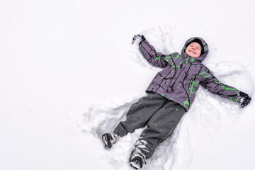 Fototapeta na wymiar Cute little kid boy in colorful winter clothes making snow angel, laying down on . Active outdoors leisure with children in . Happy child.