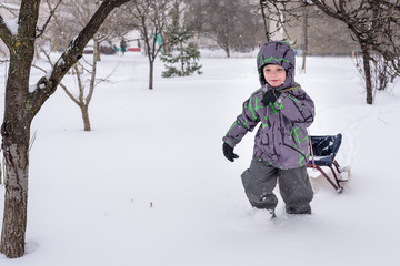Fototapeta na wymiar Happy kid walking outdoors in winter city drags his sled. child smiling and having fun.