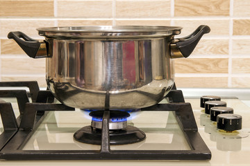 Metal cooking pot standing on kitchen stove with flame.