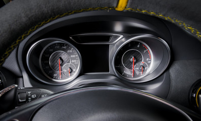 Car speedometr, black and chrome, soft light, unfocused steering wheel with yellow stitch