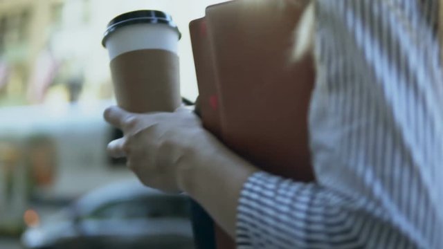 Close-up view of young businesswoman holding documents, notebooks and coffee, going to work in office. Slow motion.