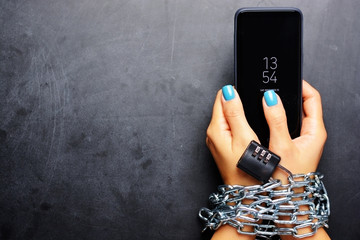 Woman hands tied with metallic chain with padlock on dark background suggesting internet or social media addiction - obrazy, fototapety, plakaty