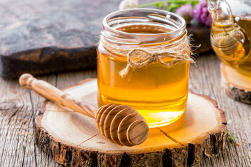 jar of honey with honey dipper on  wooden slice close-up  with teapot and flowers
