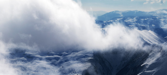 Panoramic view on winter snow mountains in sunlight clouds