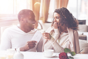 Love story. Pretty dark-skinned female keeping smile on her face covering her mouth while looking at her boyfriend
