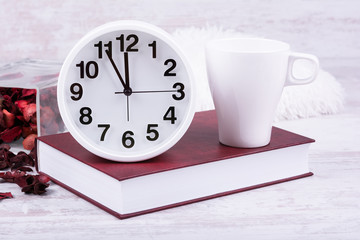 White mug mock-up. Red book, clock and mug on white wooden background.