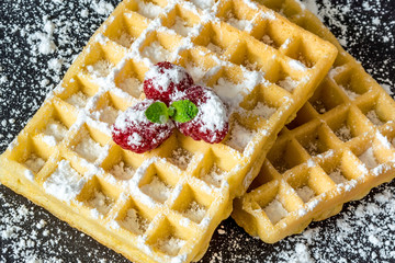Sweet toast waffles with raspberries and a sprig of mint leaves on top and sugar powder close-up...