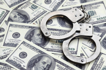 Police handcuffs lie on a lot of dollar bills. The concept of illegal possession of money, illegal...