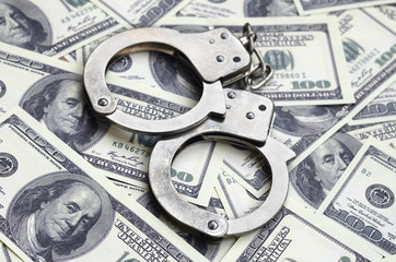 Police handcuffs lie on a lot of dollar bills. The concept of illegal possession of money, illegal...