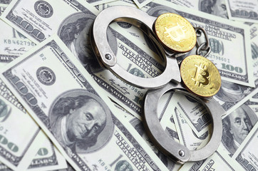 Police handcuffs and bitcoins lie on a large number of dollar bills. The concept of problems with...