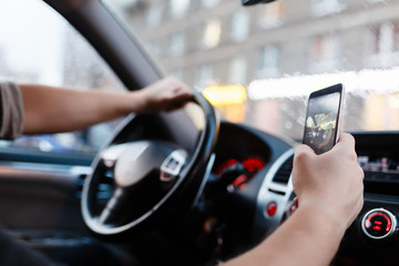Driver with a smartphone in hand in the driver's seat. The concept of inattention at the wheel. Distracted by SMS or call by mobile. The young man makes a picture by mobile phone.
