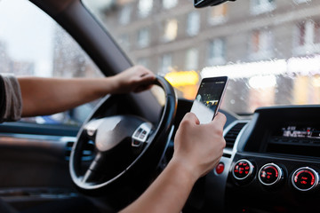 Driver with a smartphone in hand in the driver's seat. The concept of inattention at the wheel. Driving with one hand, distracted by SMS or call by mobile. Cropped hand of businessman using phone