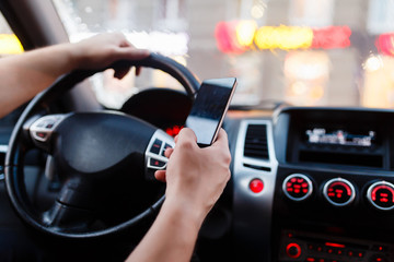 Naklejka premium Driver with a smartphone in hand in the driver's seat. The concept of inattention at the wheel. Driving with one hand, distracted by SMS or call by mobile. Cropped hand of businessman using phone