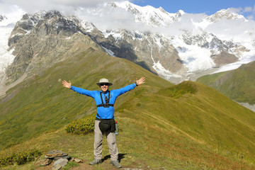 tourist with arms raised standing against a mountain landscape.