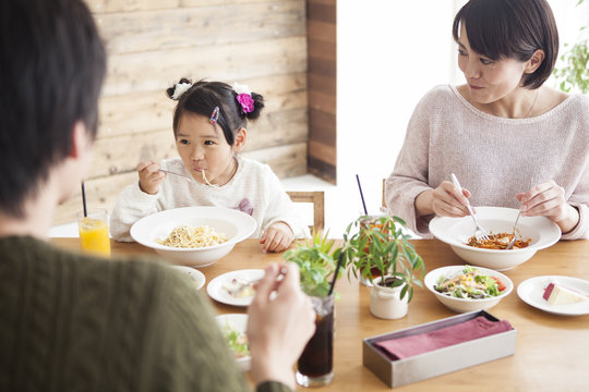 Dad, mommy and daughter are eating pasta.