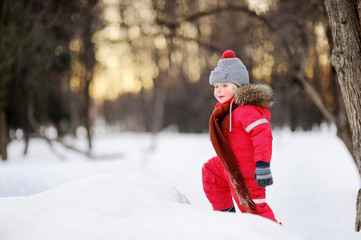 Little boy in red winter clothes having fun with fresh snow