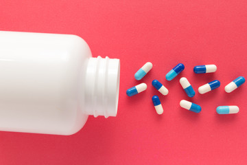Capsules spilling out of white bottle. Red background.
