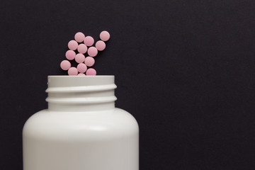 Group pink tablets. Capsules spilling out of white bottle. Black background.