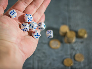 The man throws the game dice on the table with coins. Money and game cubes.