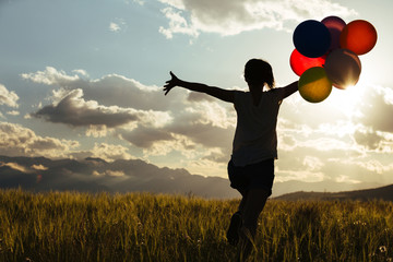 Cheering young woman running on grassland with colored balloons