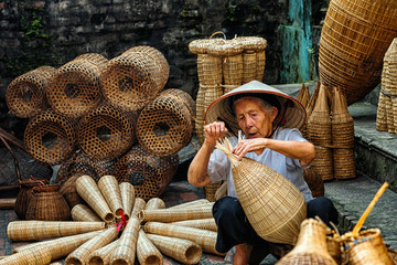 Old Vietnamese female craftsman making the traditional bamboo fish trap or weave at the old...