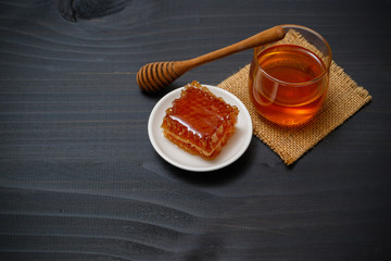 Sweet honeycomb and wooden honey dipper isolated on black wood desk.