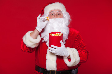 Traditional Santa Claus watching TV, eating popcorn. Christmas. Red background. emotions fear surprise