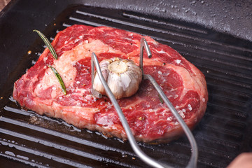 steel forceps greasing garlic beef steak, frying in black grill pan
