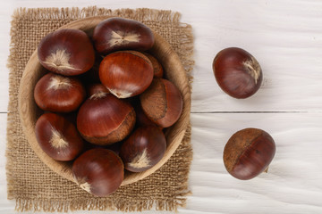 chestnut in bowl on white wooden background. Top view. Flat lay